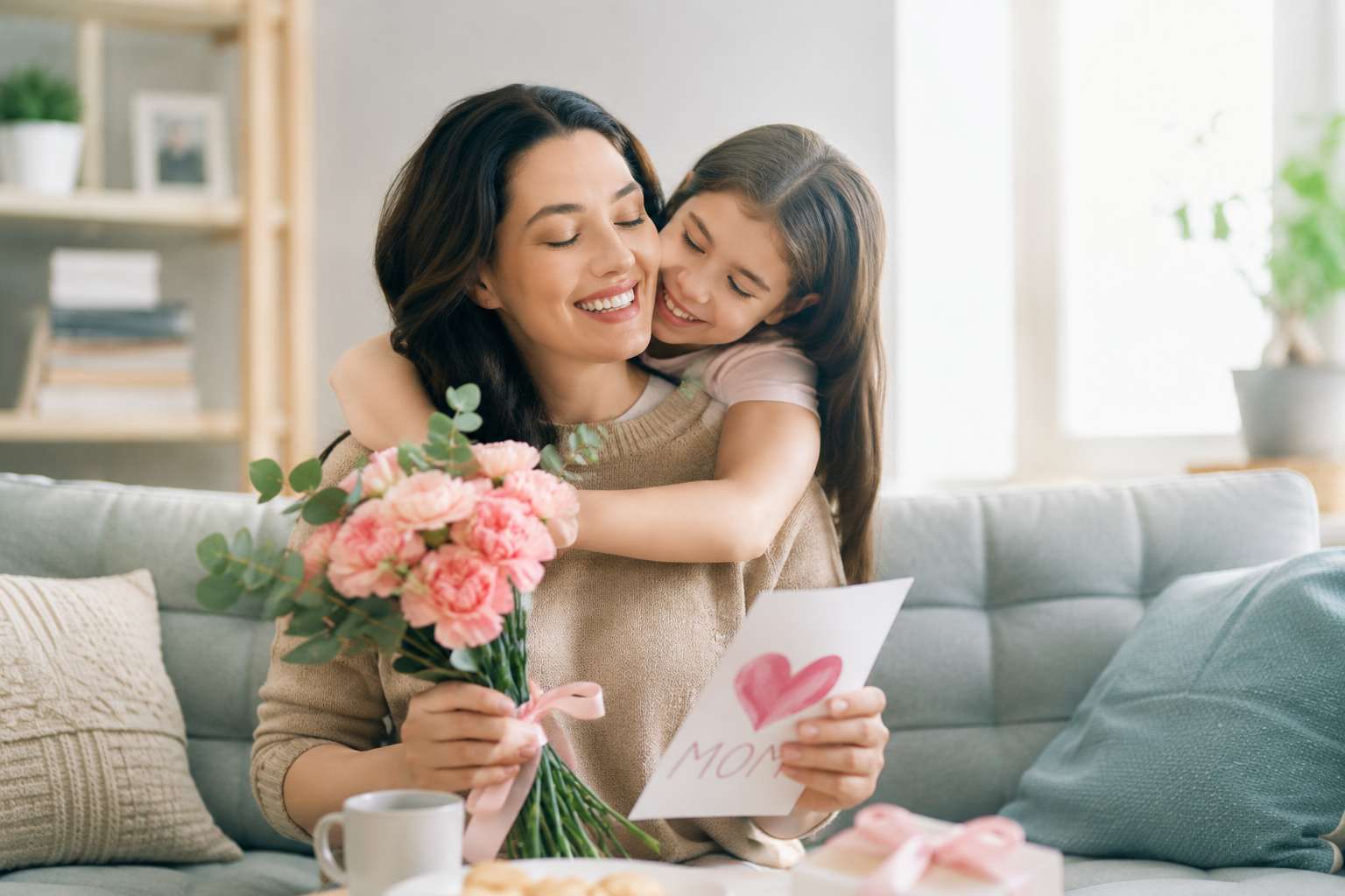 Mother receiving flowers and a handmade card from her daughter while celebrating Mother's Day at home.